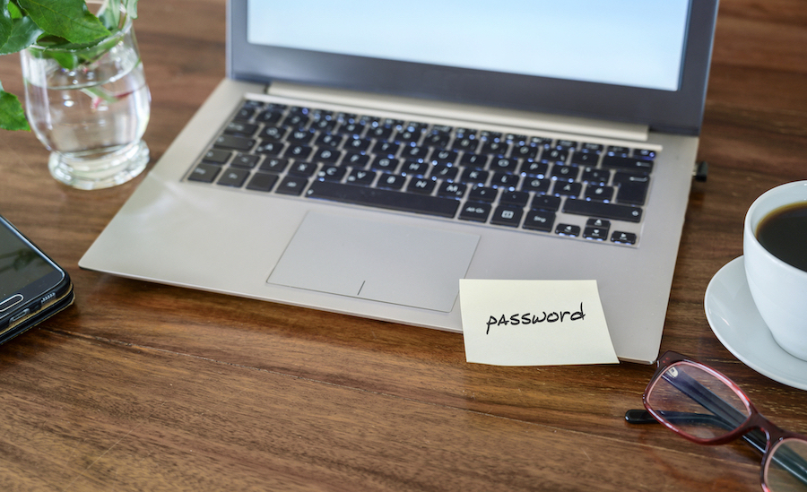 password written on a sticky note and taped to the laptop on a wooden desk, dangerous security gap, copy space, selected focus, narrow depth of field