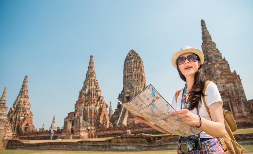 Travel Thailand Ayutthaya tourist woman on Asia sightseeing holding map with big pagoda and spectacular buddhist attraction in Wat Chaiwatthanaram. Tourism people concept with mixed race Asian girl.